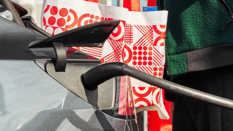 An electric vehicle charging at a Target store as a guest carries a reusable Target shopping bag.