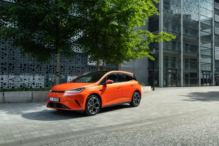 Orange BYD DOLPHIN G DM-i plug-in hybrid supermini parked outside a modern building