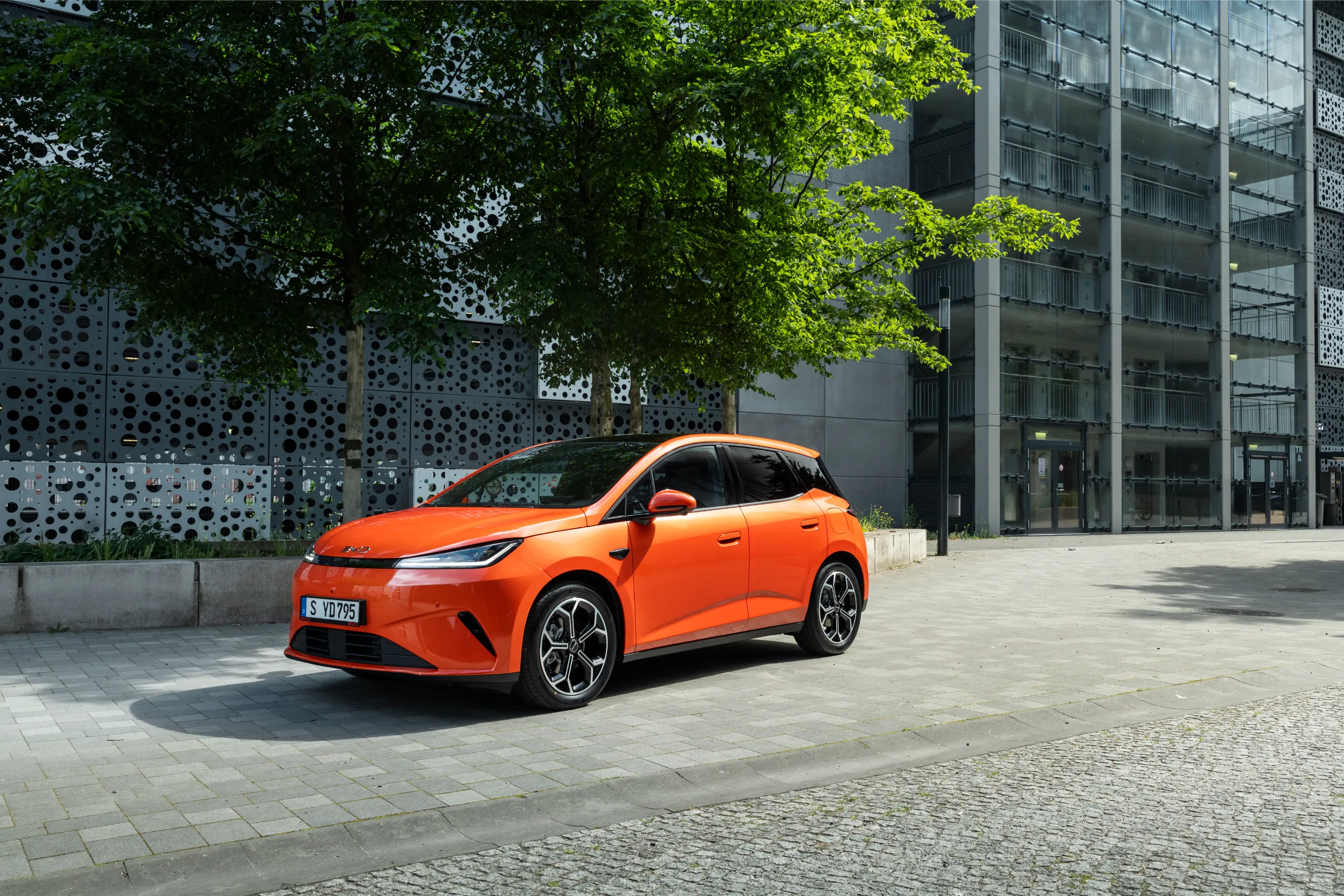 Orange BYD DOLPHIN G DM-i plug-in hybrid supermini parked outside a modern building