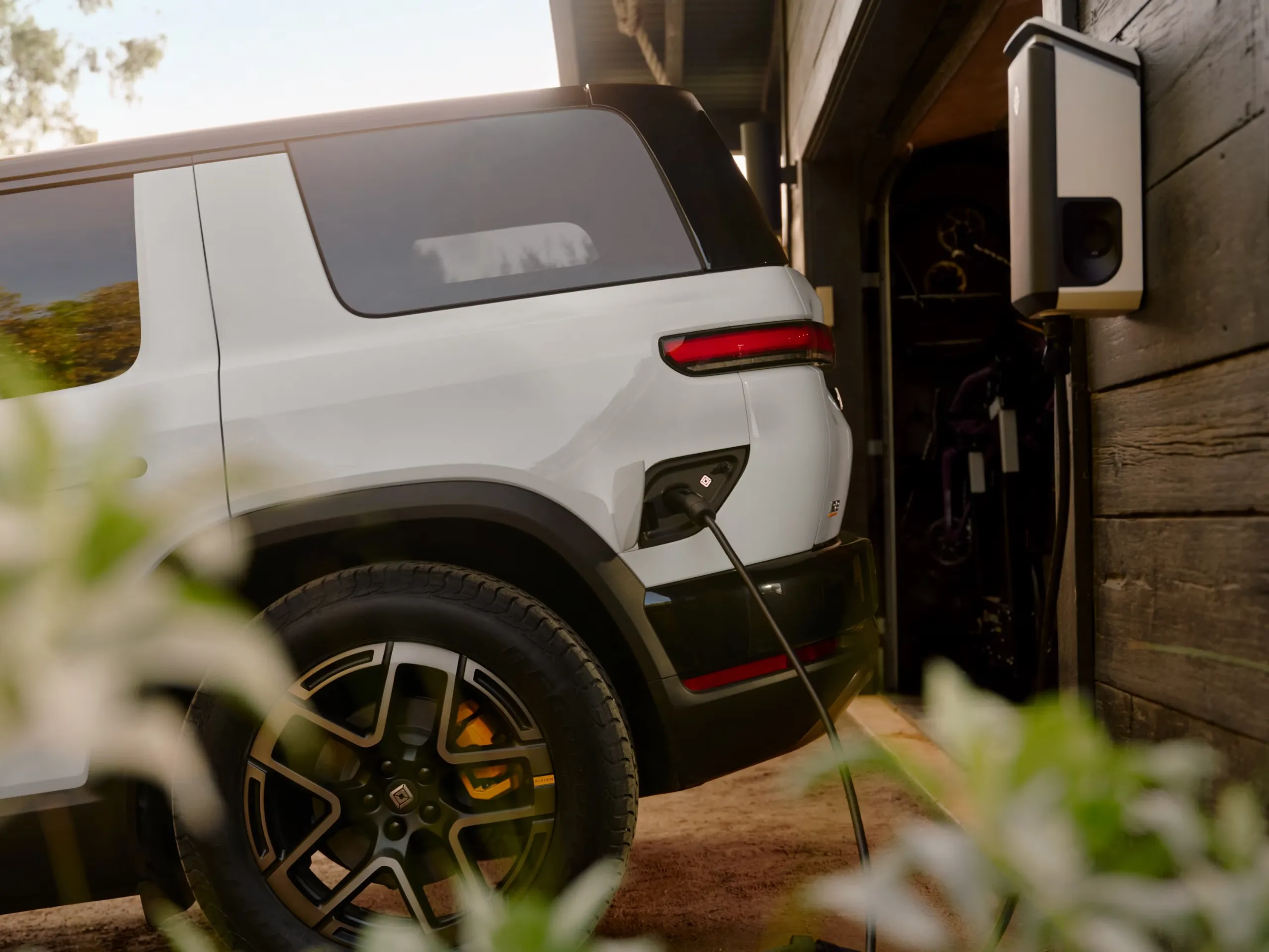 Rivian R2 electric SUV parked at a home charging setup in a residential driveway