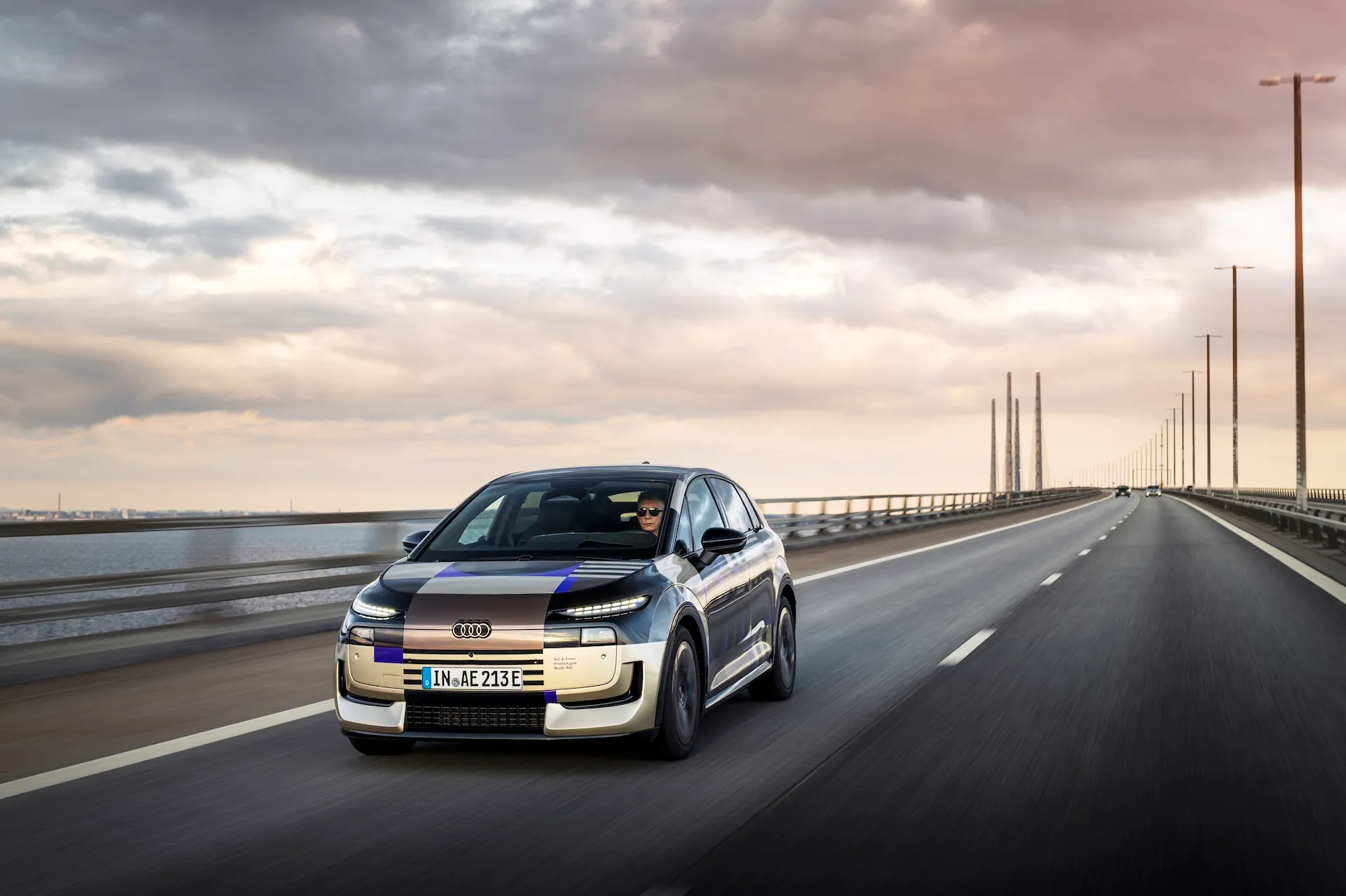 Audi A2 e-tron with design livery driving on an open road, front three-quarter exterior view of the compact electric model.