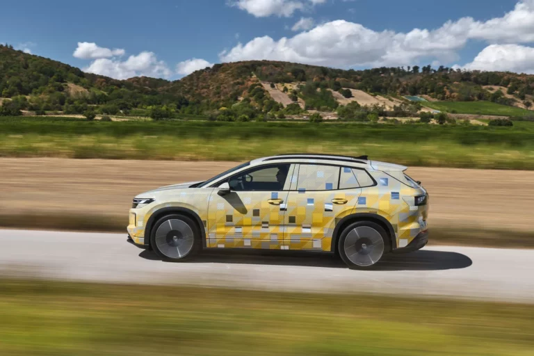 Camouflaged Volkswagen ID. Tiguan prototype driving on a rural road with wind turbines in the background