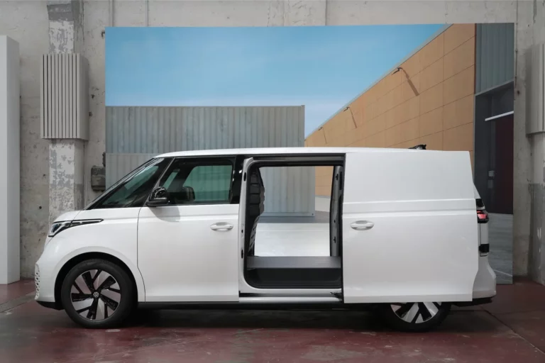 White Volkswagen ID. Buzz Cargo long wheelbase electric van in side profile with its sliding door open, showing the wooden load floor.
