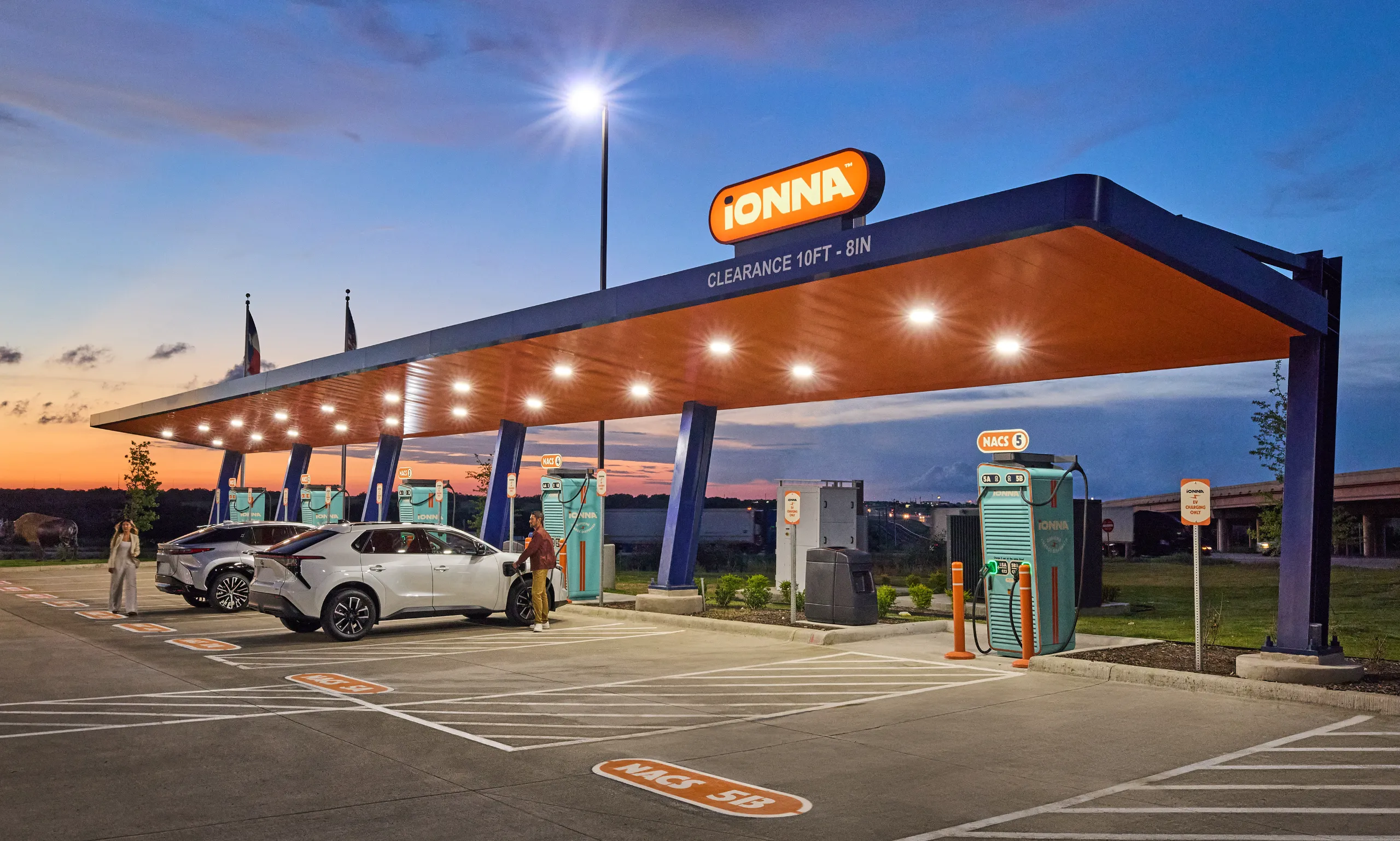 IONNA charging network Rechargery at dusk, with SUVs parked at NACS fast chargers beneath an illuminated canopy