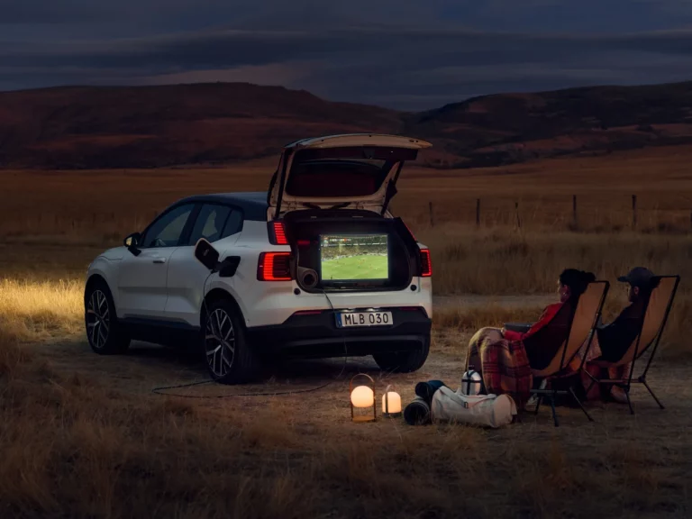White Volvo EX30 parked at dusk with its rear hatch open, powering devices at a campsite using V2L capability