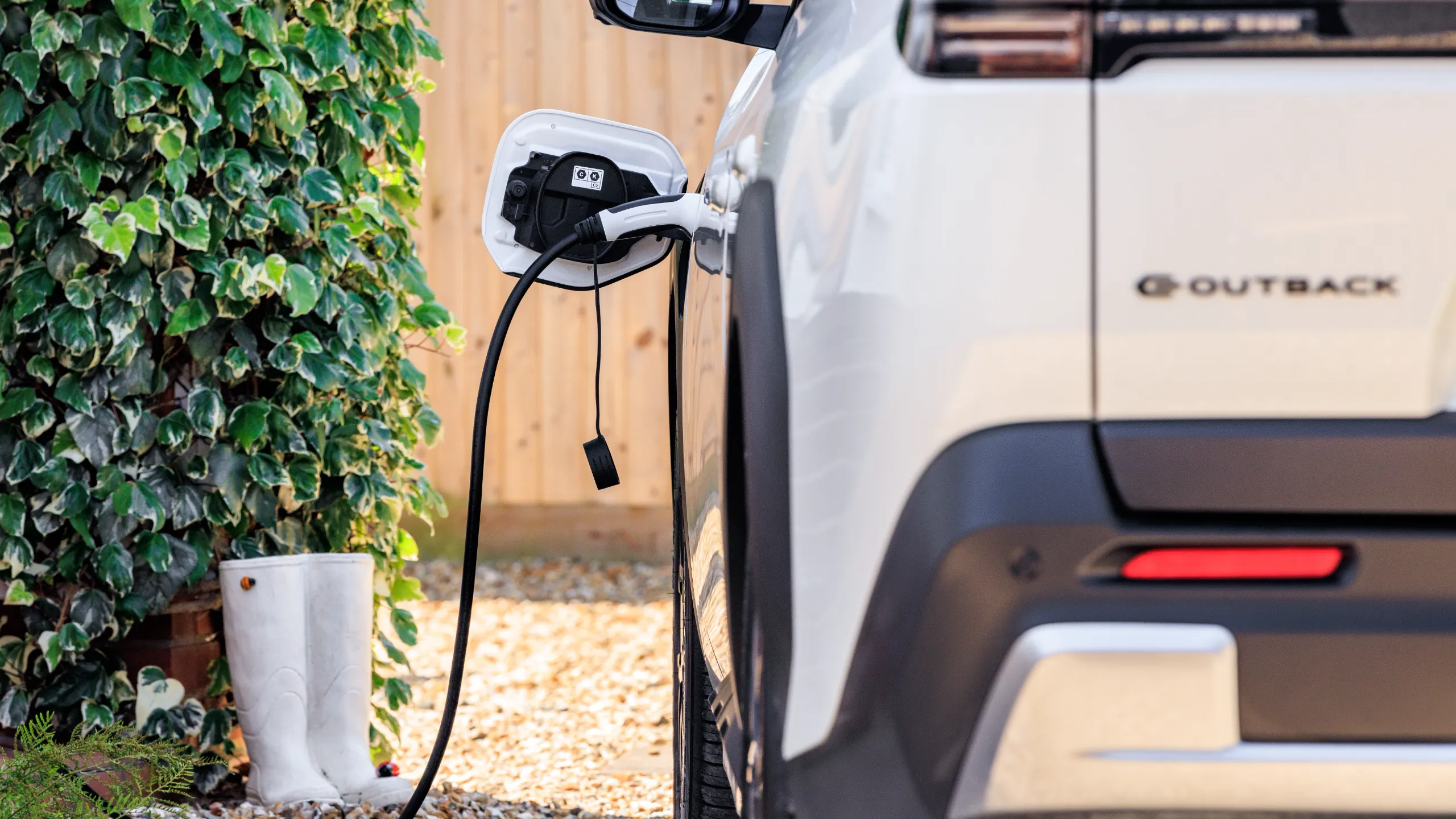 White Subaru E-Outback electric SUV plugged into a home charger, illustrating Subaru Europe's EV rollout alongside its MUFG Green Deposit placement